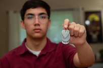 Henry Maxwell poses for a photo with family heirloom dog tags, March 22, 2025. Maxwell was accepted to the U.S. Naval Academy and will become a midshipman in June joining the class of 2029. (U.S. Navy photo taken by Mass Communication Specialist 1st Class Ryan Riley)