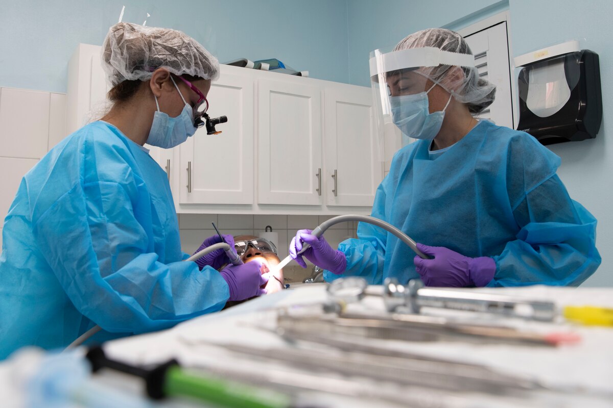 Two military members providing dental treatments during a tooth filling.