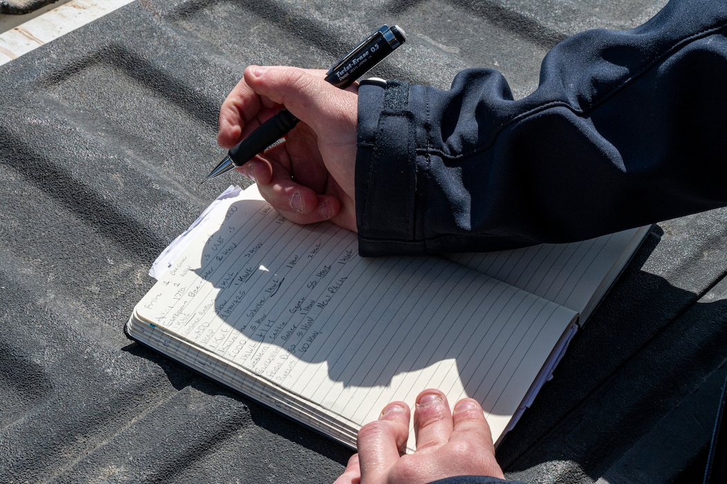 A pair of hands into frame holding a pen writing in a notebook