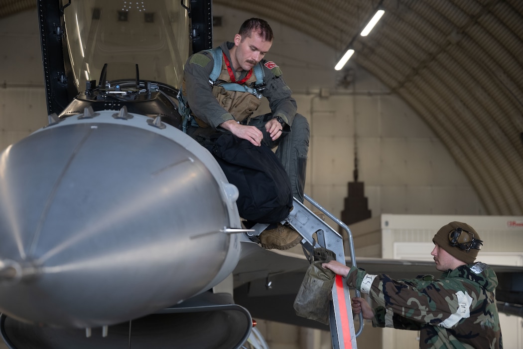 A fighter pilot and a mechanic wearing a hazmat suit conduct pre-flight checks on a F-16 fighter jet.