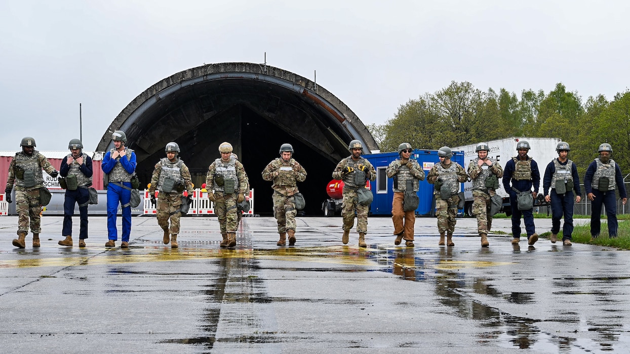 Airmen in full combat kit standing shoulder to shoulder walk length-wise along a taxiway.