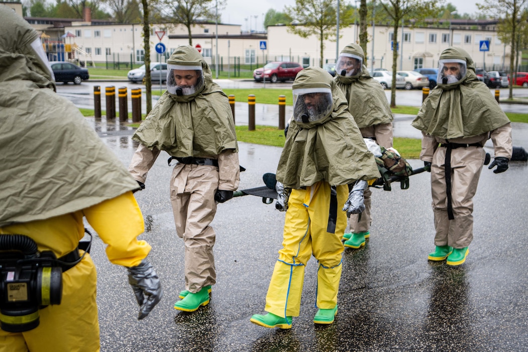 Airmen in hazmat suits carry a patient on a litter.
