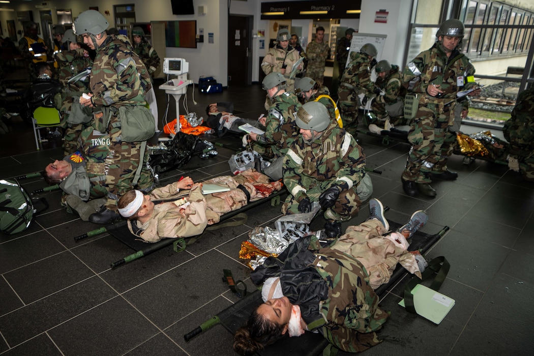 Military medics in hazmat suits triage patients on litters in the lobby of a clinic.