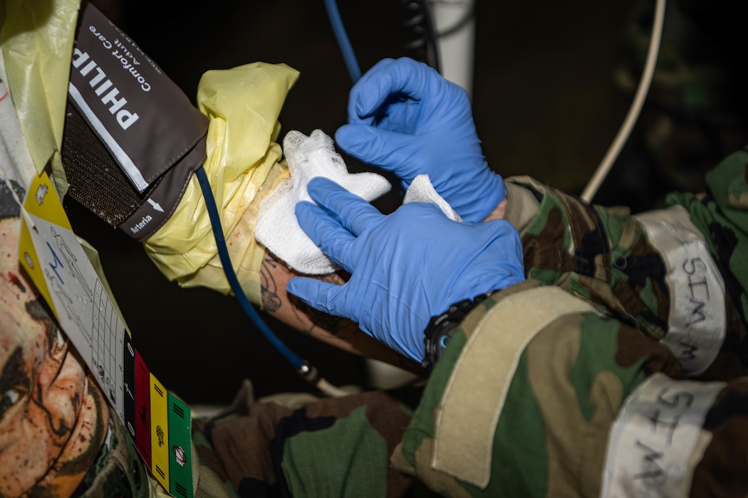 A miliary medic in a hazmat suit presses gauze into a patient's wound.