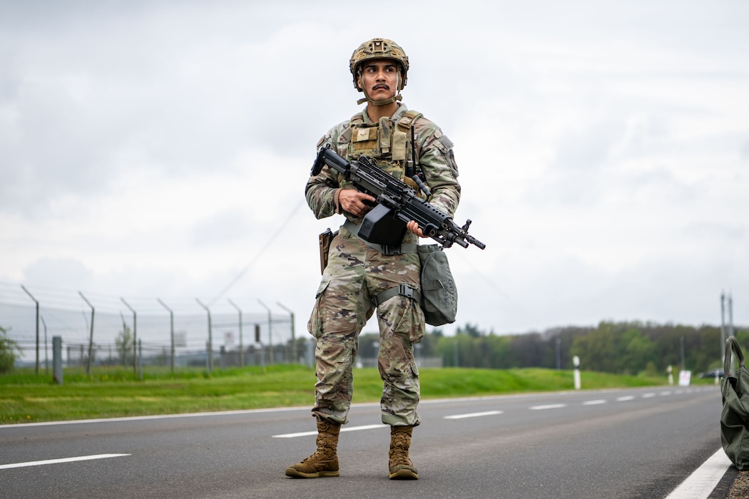 A military policeman in a protective vest and helmet holds a weapon and pulls security on a road.