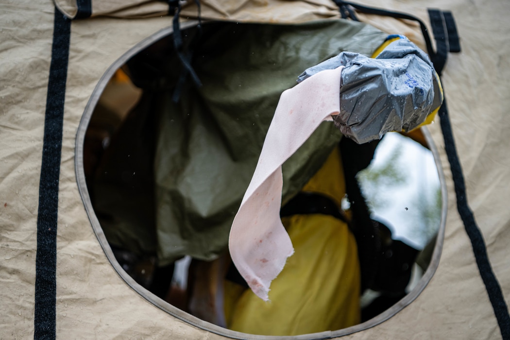 An Airman in a hazmat suit sticks their arm outside of a tent while holding a used bandage.