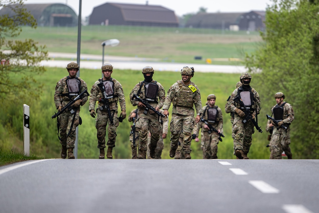 Military policeman carrying weapons walk down a road