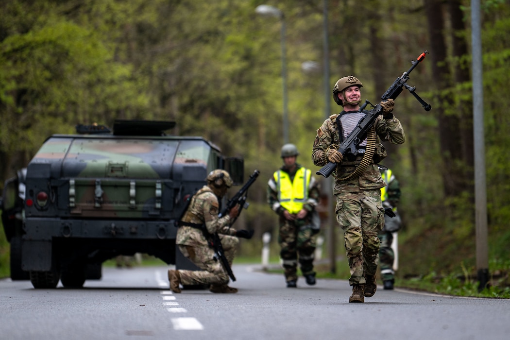 A military policeman in combat gear and a hazmat suit carries a weapon down the road.