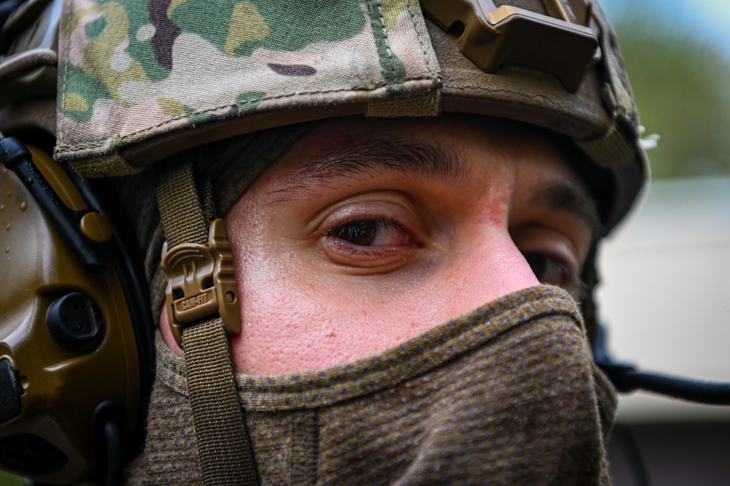 A military policeman wearing a ski mask and a tactical helmet looks into the frame.