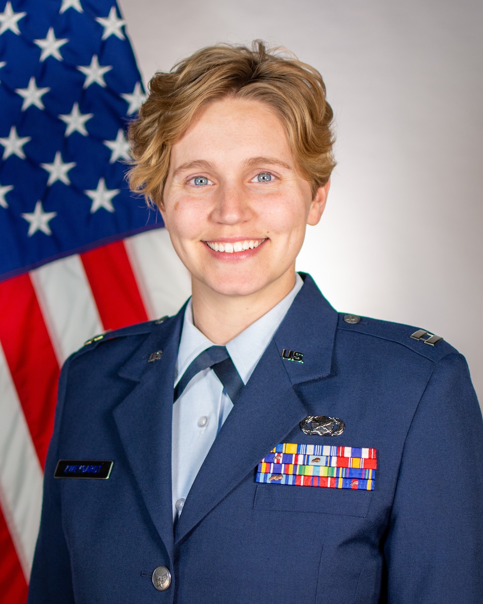 Service member smiles for official portrait in front of US flag wearing their service dress blues