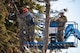 Two Airmen cut branches off a tree.