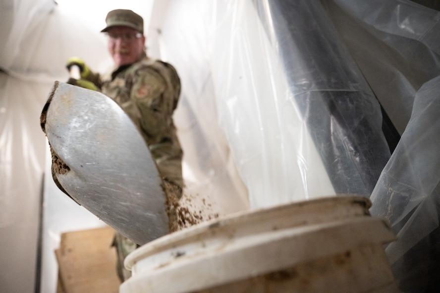 An Airman shovels broken-up concrete into a bucket.