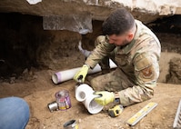 An Airman prepares PVC pipes inside a hand-excavated command suite.