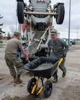An Airman transports wet concrete in a wheelbarrow.