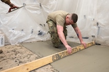 An Airman screeds concrete.