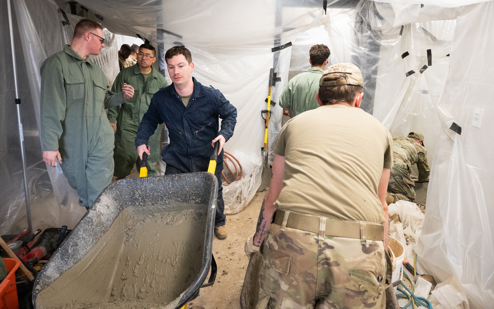 Airmen wheel concrete in and out of a building.