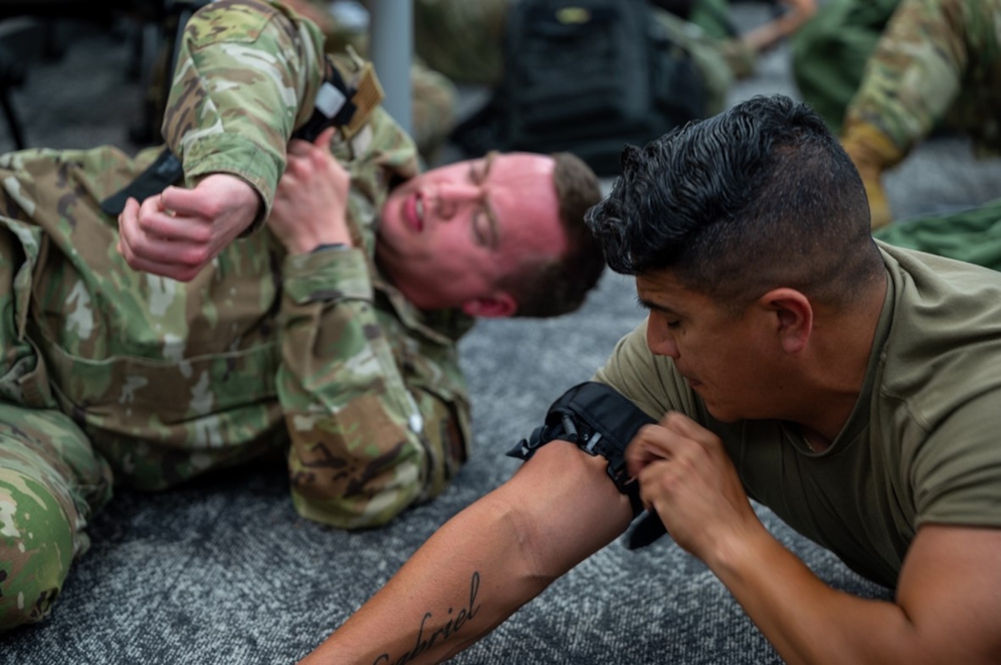 Two Airmen tie band to arm on the floor. (U.S. Air Force photo by Airman 1st Class Donnell Ramsey)
