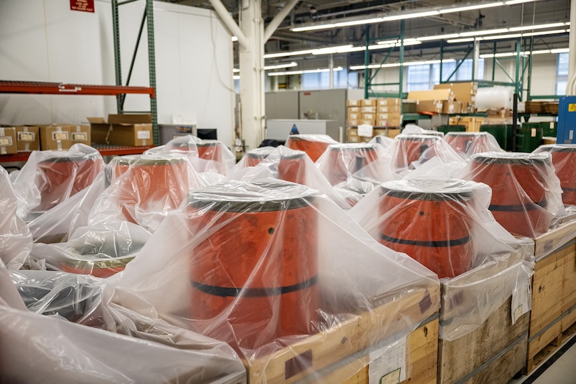 Several orange cylindrical tanks are covered in plastic wrapping in a warehouse.