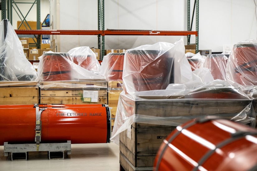 Several orange cylindrical tanks are in a warehouse; several are covered in plastic wrapping.