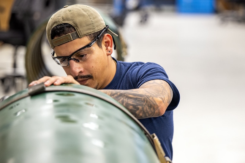 A man in a blue shirt looks at the end of a large green cylindrical tank.