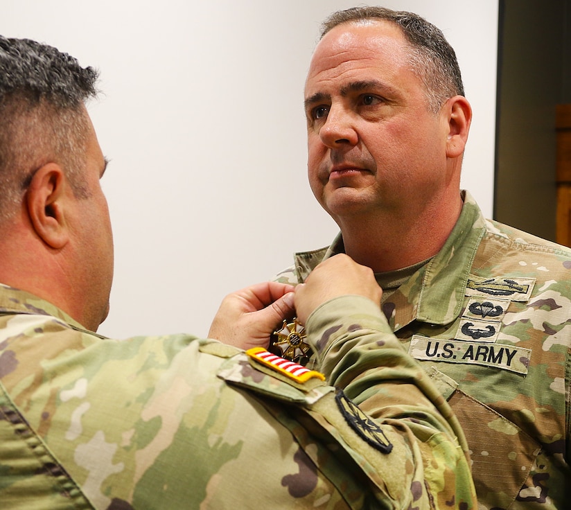 Col. Shawn Nokes, Commander of the 129th Regiment (Regional Training Institute) affixes the Legion of Merit on the collar of Command Sgt. Maj. Jonathan Genisio.