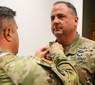 Col. Shawn Nokes, Commander of the 129th Regiment (Regional Training Institute) affixes the Legion of Merit on the collar of Command Sgt. Maj. Jonathan Genisio.