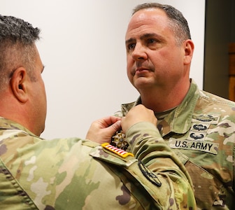 Col. Shawn Nokes, Commander of the 129th Regiment (Regional Training Institute) affixes the Legion of Merit on the collar of Command Sgt. Maj. Jonathan Genisio.