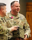 Col. Shawn Nokes, Commander of the 129th Regiment (Regional Training Institute) presents an ammo box with all of the crests of the units that Command Sgt. Maj. Jonathan Genisio has served in to the command sergeant major during his April 26 retirement ceremony.
