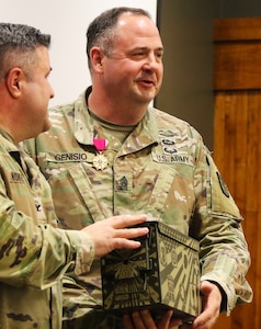 Col. Shawn Nokes, Commander of the 129th Regiment (Regional Training Institute) presents an ammo box with all of the crests of the units that Command Sgt. Maj. Jonathan Genisio has served in to the command sergeant major during his April 26 retirement ceremony.