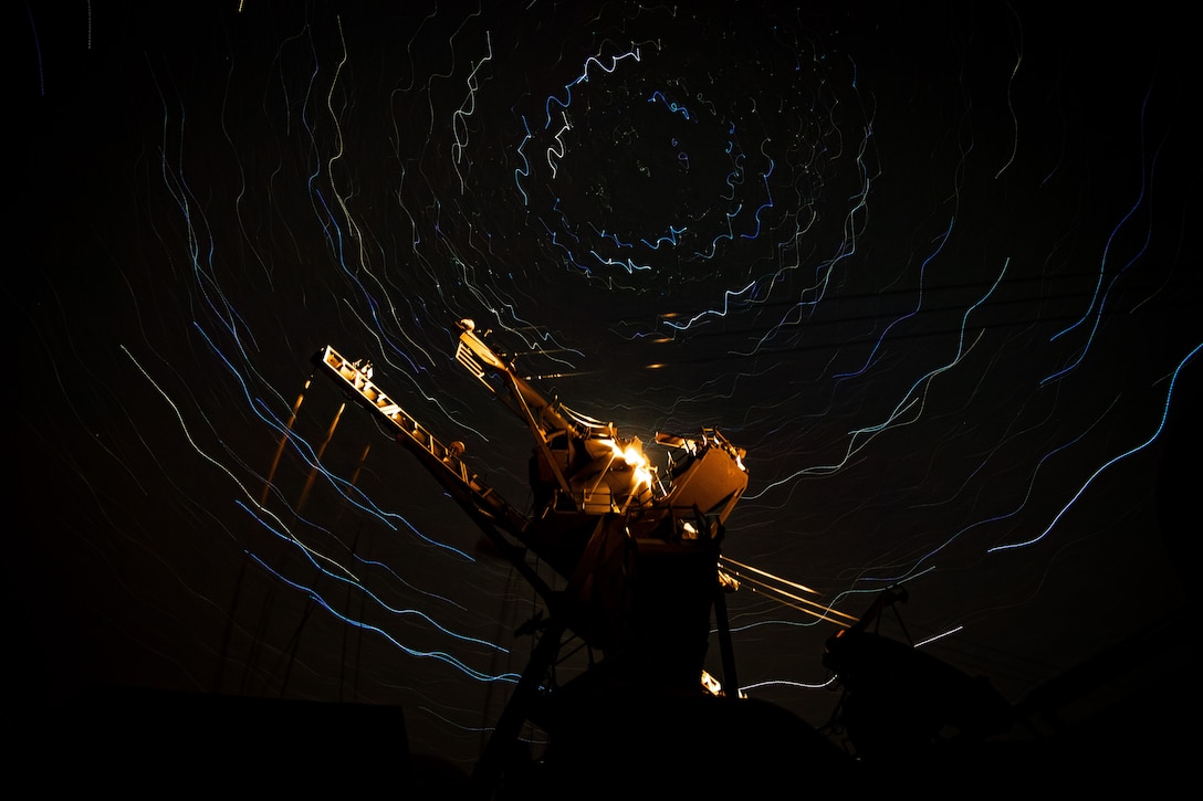 An illuminated ship sails at night in a sea with luminescent squiggly, circular lines.