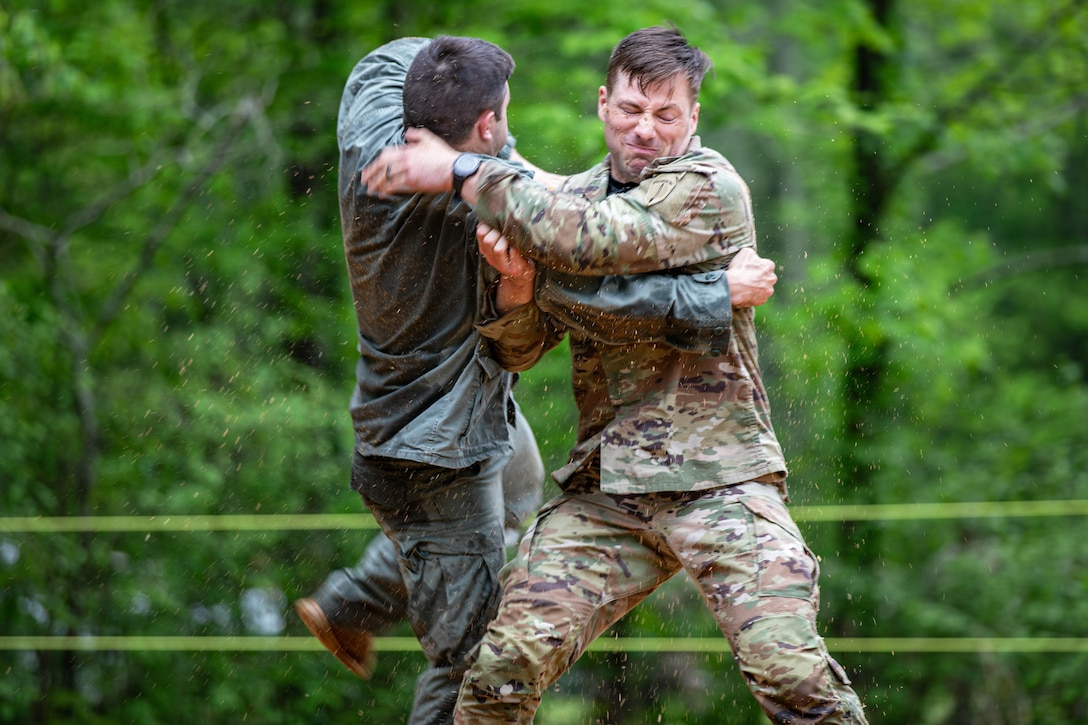 Two soldiers in uniform engage in hand-to-hand combat with green trees in the background.