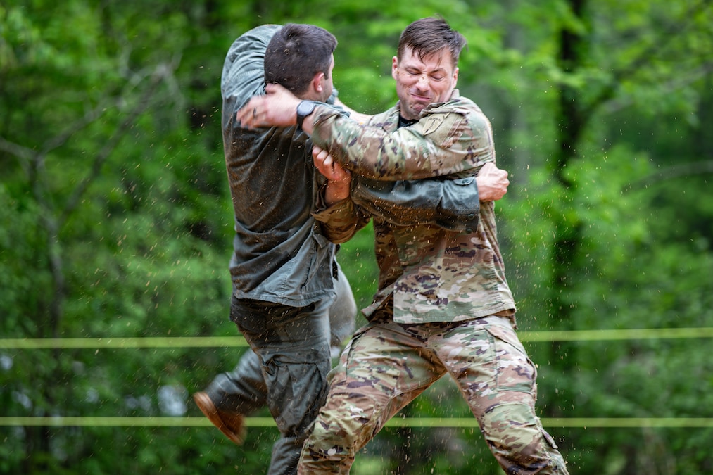 Two soldiers in uniform engage in hand-to-hand combat with green trees in the background.