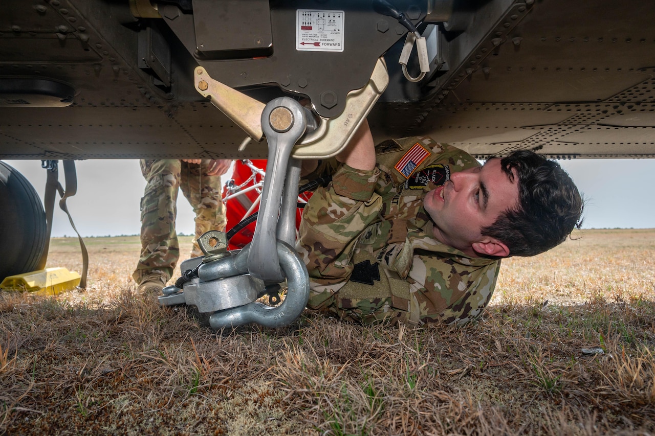 A guardsman works underneath a helicopter to attach a bucket firefighting system.