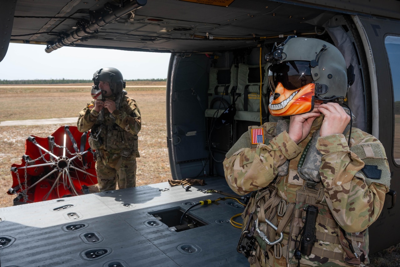 Two guardsmen put on helmets next to a parked helicopter.