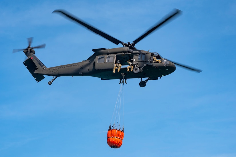 A Black Hawk carries a bucket filled with water while in flight.