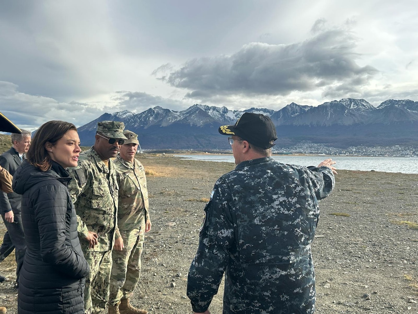 A man in a military uniform points to a waterway while a three people look on.