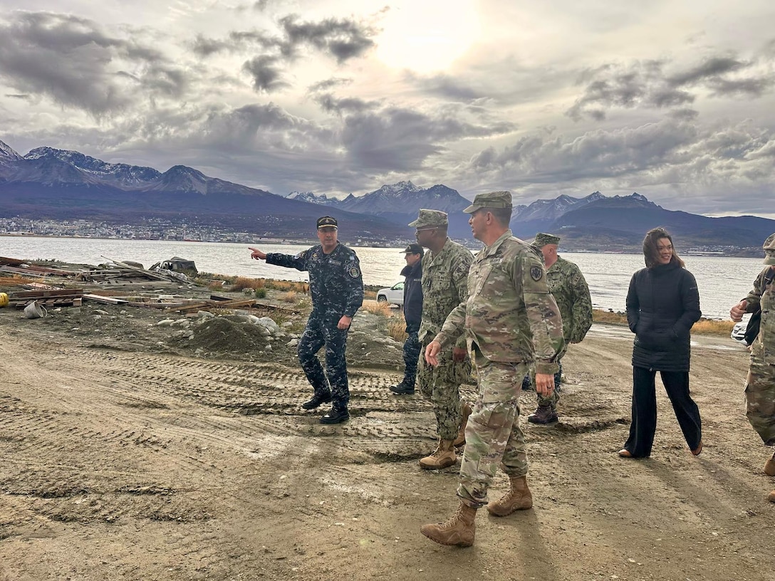 A group of military leaders walk with a waterway in the background.