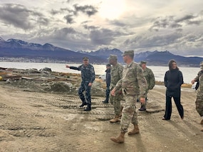 A group of military leaders walk with a waterway in the background.