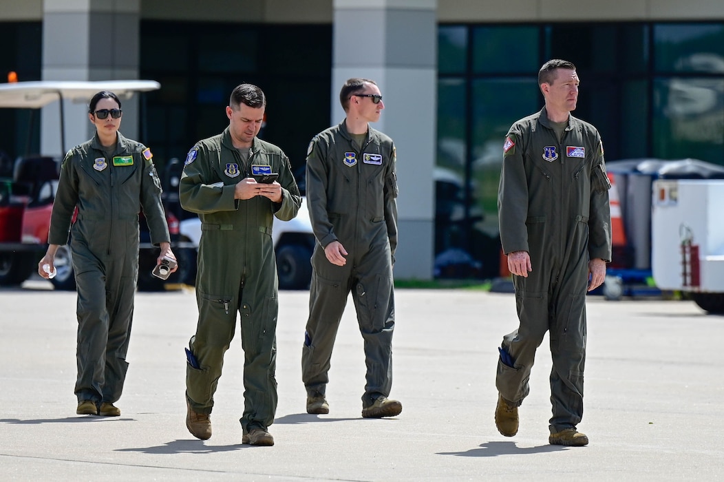A group of people walk across a flightline.