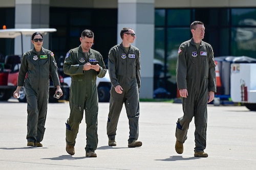 A group of people walk across a flightline.