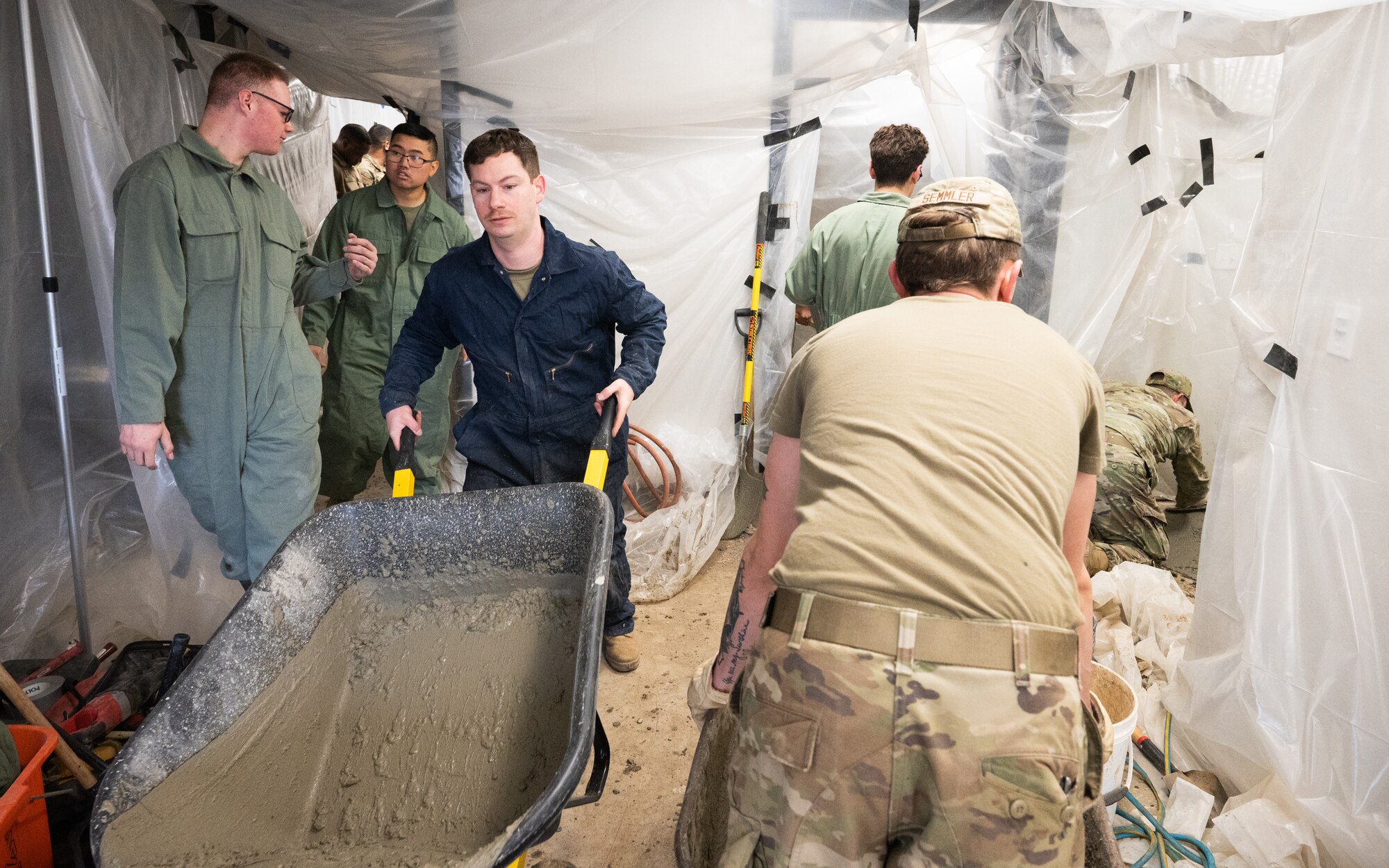 Airmen wheel concrete in and out of a building.