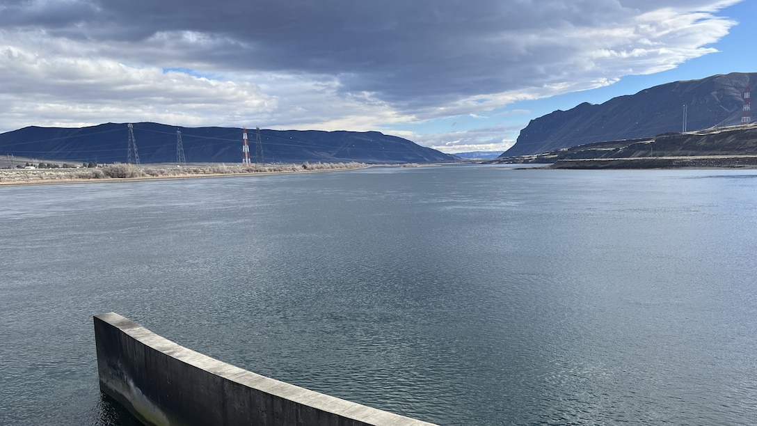 A view of a body of water with rugged hills in the background and power lines going over the river.