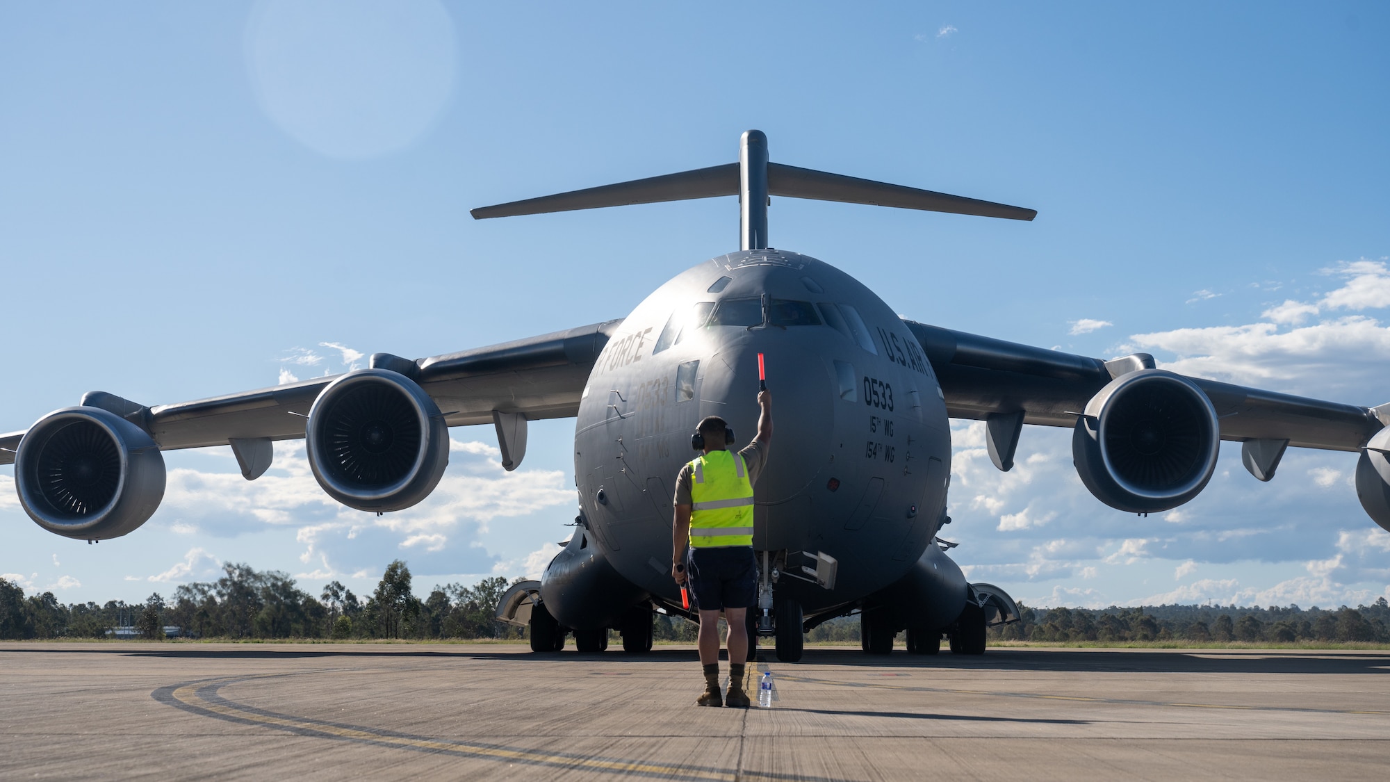 A U.S. Air Force Airmen guides a C-17 to its designated parking spot in Brisbane, Queensland, Australia.