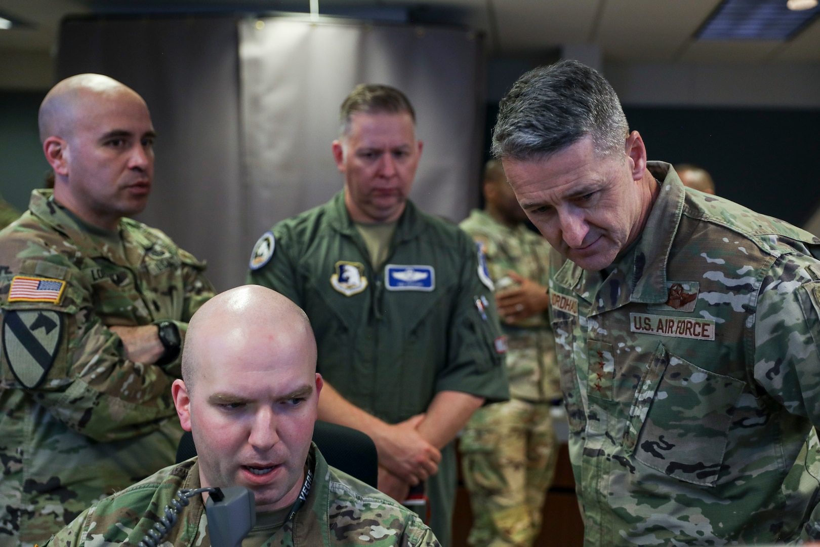 One soldier sits speaking into a handheld phone while three others stand around him looking at something off camera.