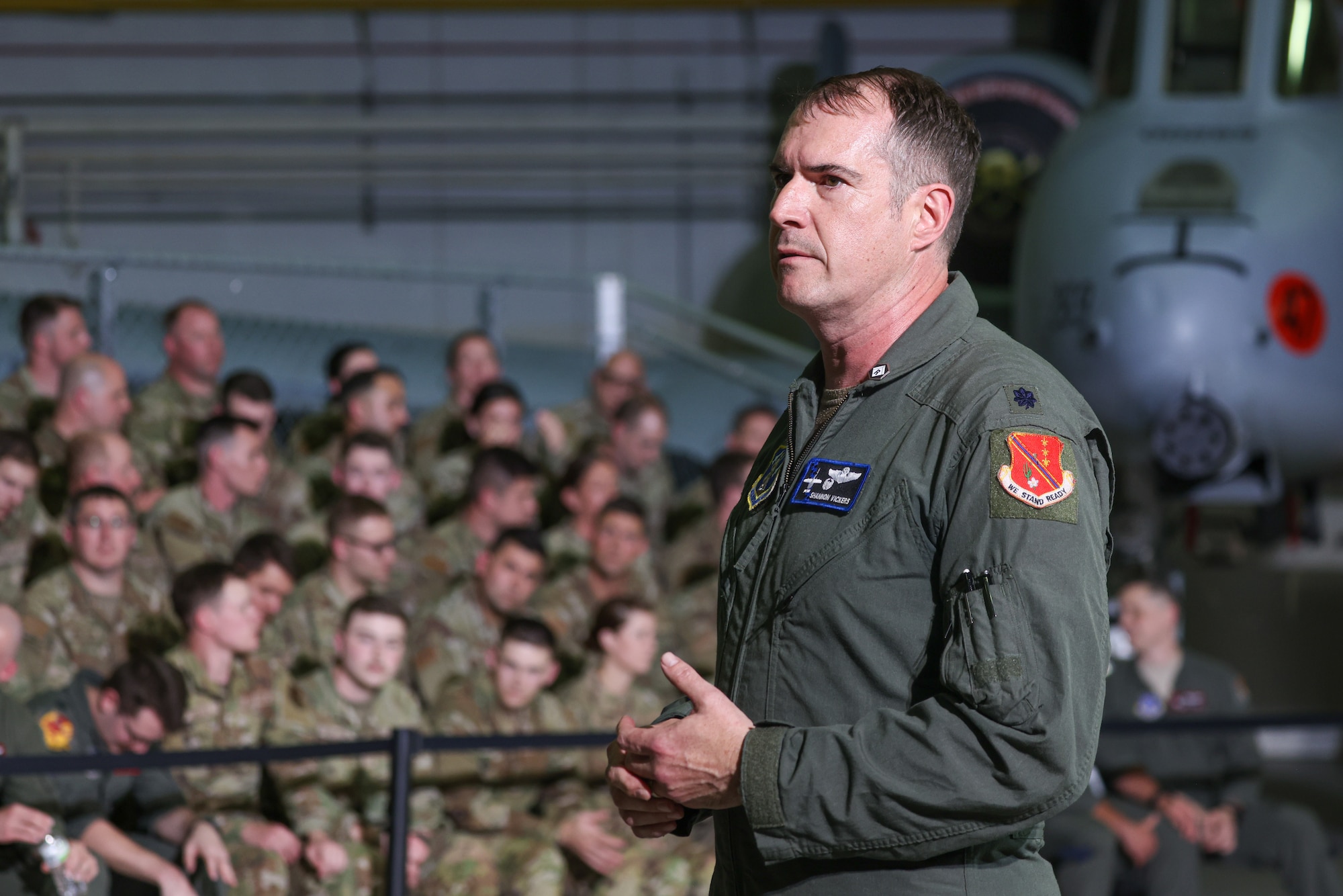 Officer in flight suit address audience of servicemembers