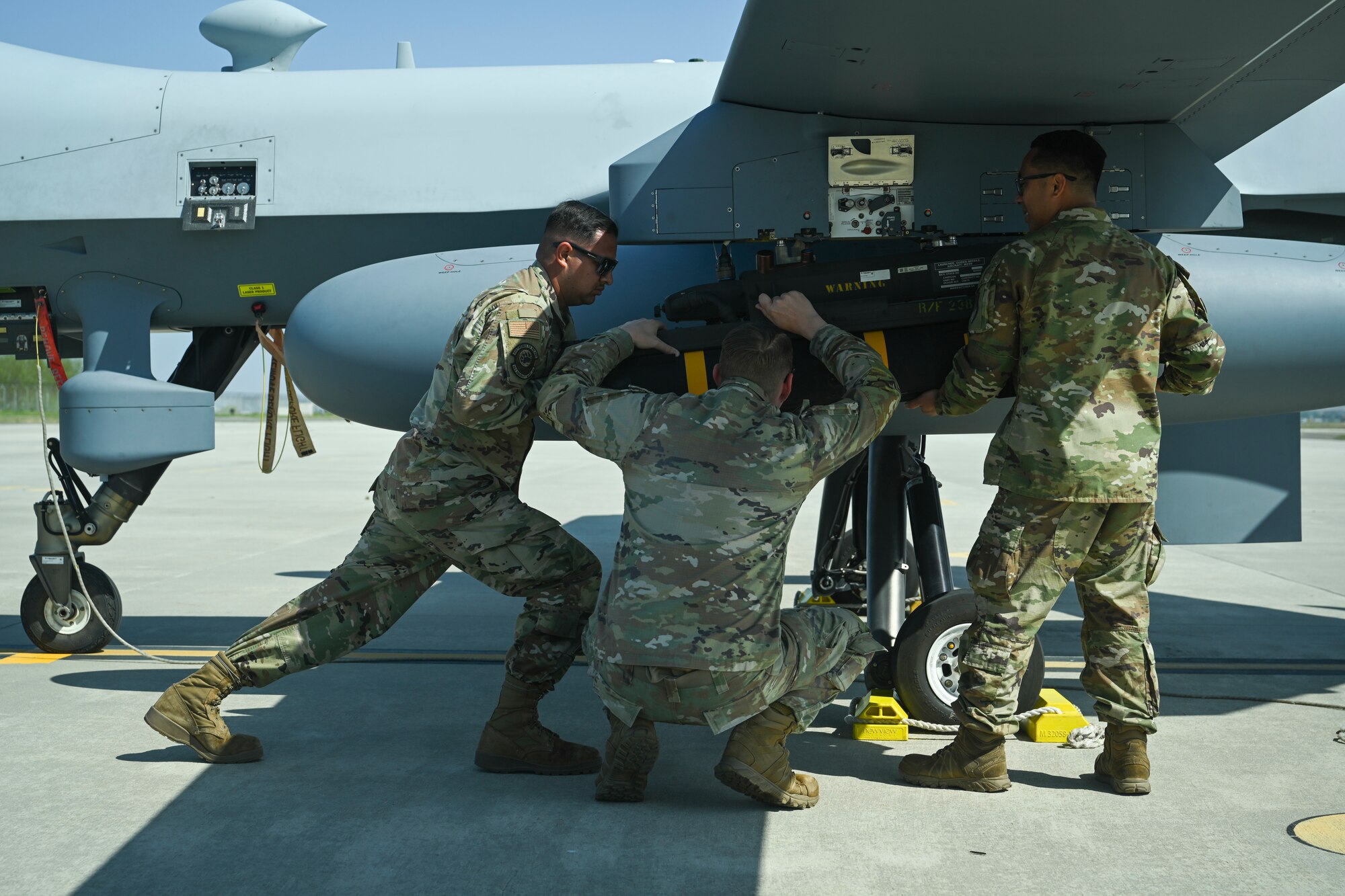 Senior Airman Eduardo Ledezma, left, Tech. Sgt. Kristopher Speir, center, and Tech Sgt. Aldrich Aldana, 163d Attack Wing MQ-9 Reaper armament systems specialists, load an AGM-114 Hellfire missile onto an MQ-9 Reaper at Kunsan Air Base.