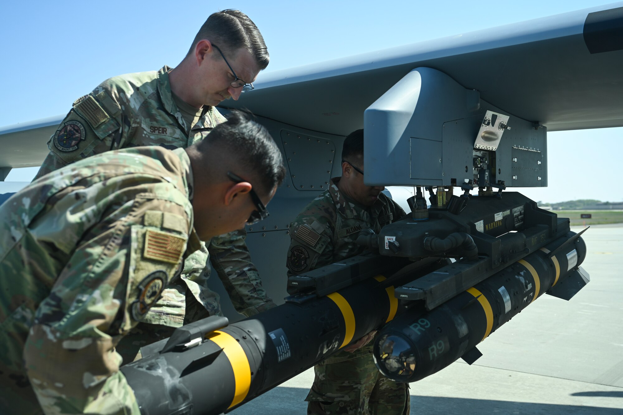 Senior Airman Eduardo Ledezma, left, Tech. Sgt. Kristopher Speir, center, and Tech Sgt. Aldrich Aldana, 163d Attack Wing MQ-9 Reaper armament systems specialists, load an AGM-114 Hellfire missile onto an MQ-9 Reaper at Kunsan Air Base.