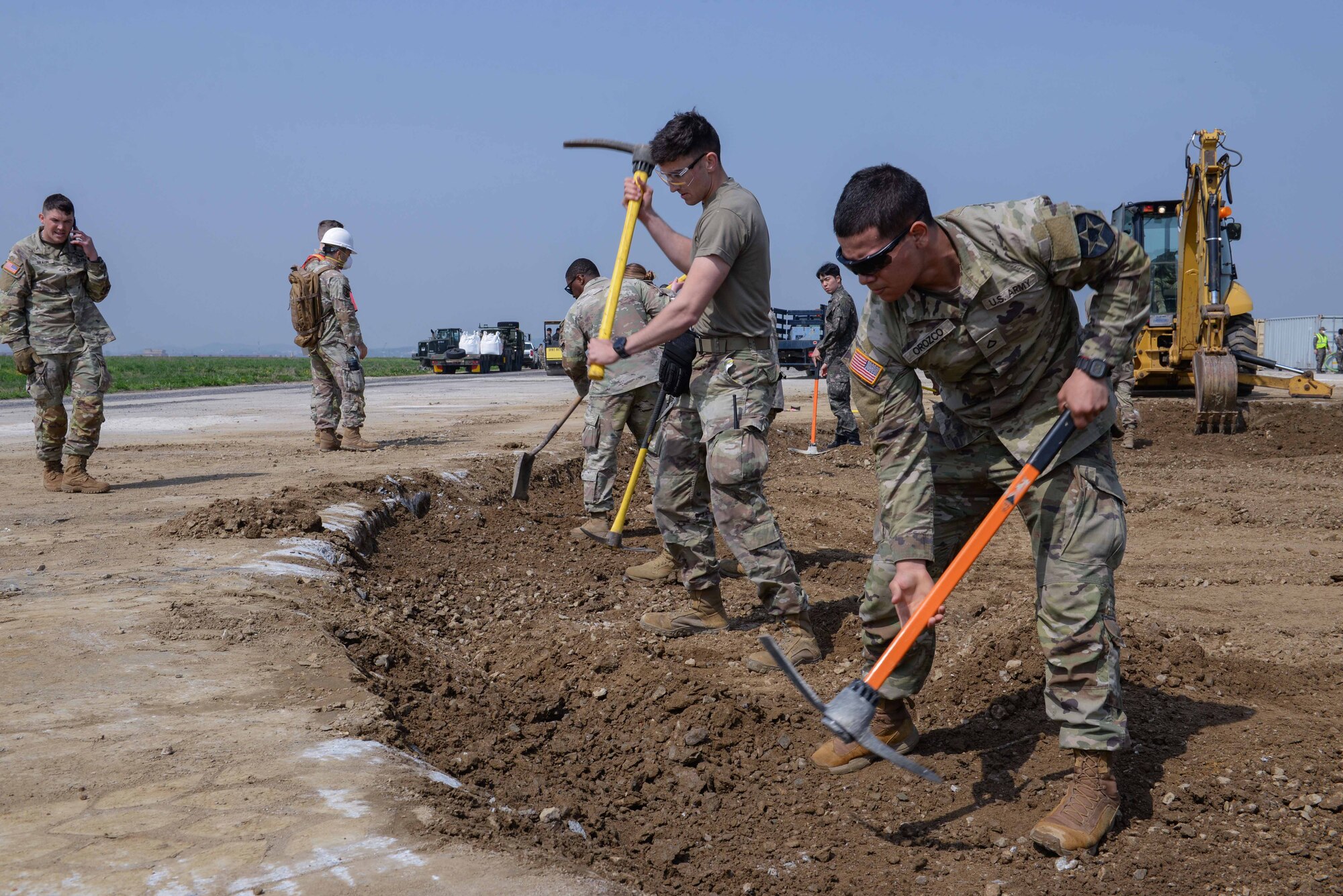Members of the U.S. Air Force, U.S. Army, Republic of Korea Air Force and ROK Army loosen rock material in a large crater during IRON RADR at Osan Air Base, Republic of Korea, April 24, 2025.  During the exercise, one large and six small craters were restored using legacy and rapid airfield damage repair techniques. IRON RADR is the first complex, joint and combined exercise on Osan AB that tests, evaluates and prepares civil engineers to safely conduct RADR operations in a simulated contingency environment. (U.S. Air Force photo by Staff Sgt. Kahdija Slaughter)