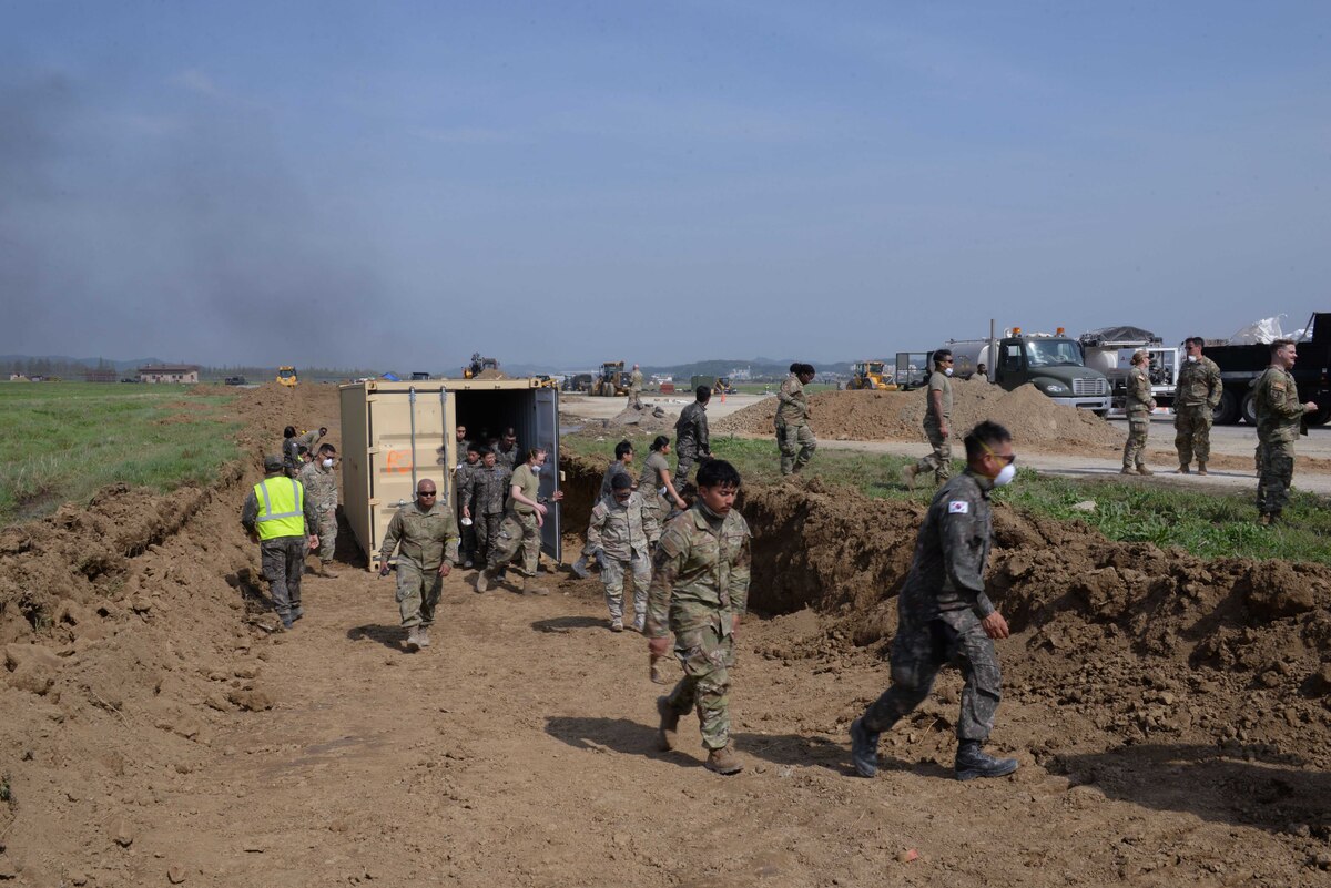 Members of the U.S. Air Force, U.S. Army, Republic of Korea Army, and ROK Air Force exit a cargo container after receiving an all clear notification during IRON RADR at Osan Air Base, Republic of Korea, April 24, 2025. Rapid airfield damage repair is a process for repairing structural damage on airfields, quickly restoring combat airpower generation when needed. Force protection solutions implemented during the exercise included v-ditches, berms, and cargo containers. (U.S. Air Force photo by Staff Sgt. Kahdija Slaughter)