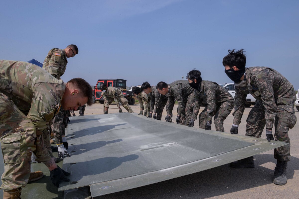 Members of the U.S. Air Force, U.S. Army, Republic of Korea Army, and ROK Air Force construct a fiber reinforced polymer mat during IRON RADR at Osan Air Base, Republic of Korea, April 24, 2025. Rapid airfield damage repair is a rapid process for repairing structural damage on airfields, quickly restoring combat airpower generation when needed. The exercise included preparing and burying temporary shelters while teams of engineers collaboratively worked to restore the airfield and simultaneously respond to several simulated attack scenarios. (U.S. Air Force photo by Staff Sgt. Kahdija Slaughter)